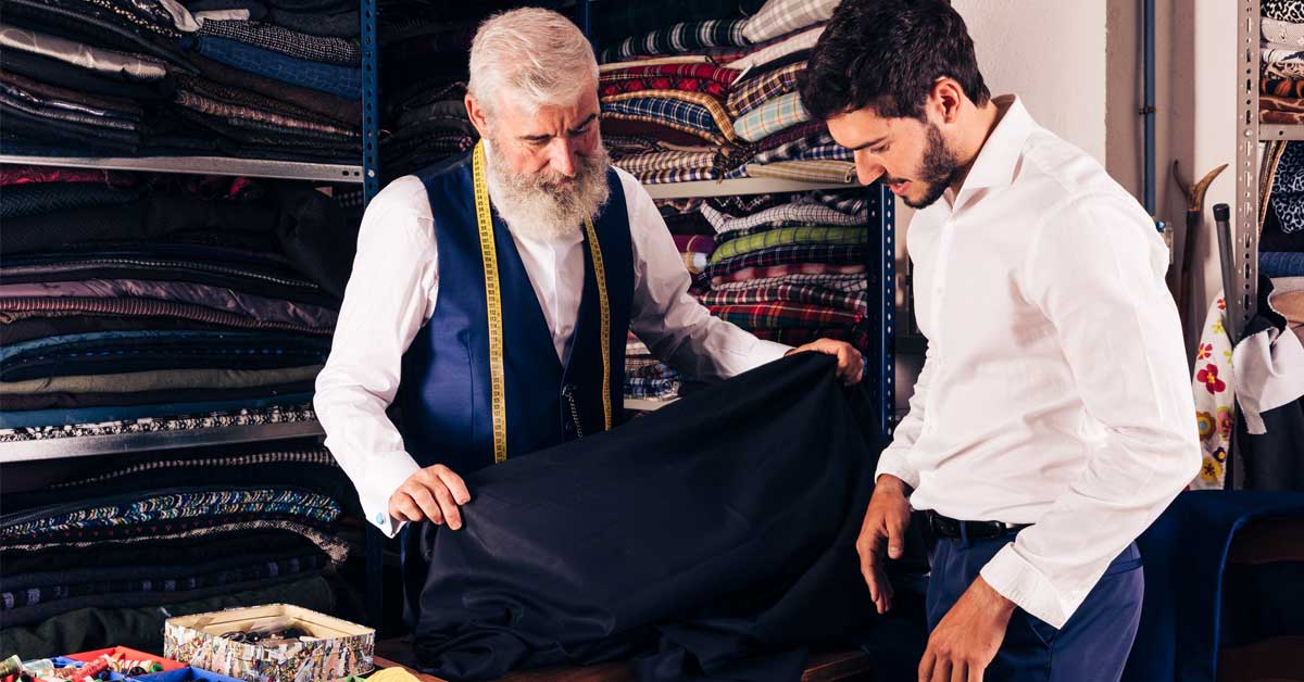 seller displaying blue fabrics to young customer in textile shop. Custom suits. Tailoring. Suits tailor. Gents tailor