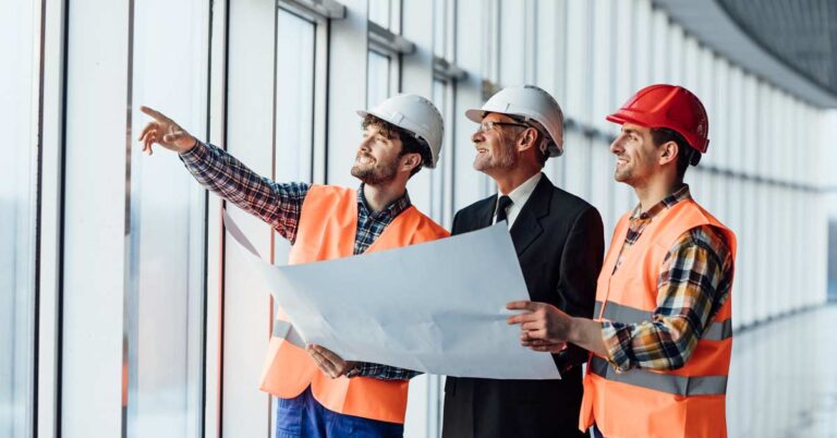 An aged construction business owner standing between two engineers in a glass building holding a map.