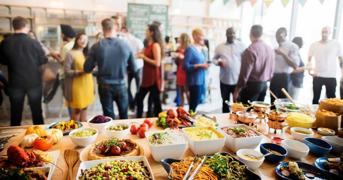 A picture of people networking at an event, with a table full of food items in front.