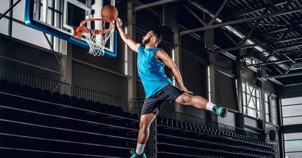 An image showing indoor basketball court with a male sportsman doing dunk.