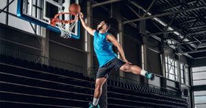 An image showing indoor basketball court with a male sportsman doing dunk.