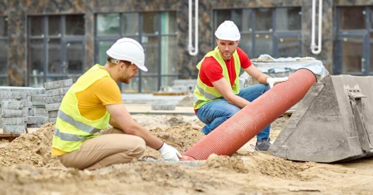 Two repairmen are performing a pipe relining service, by inserting a pipe in the ground.