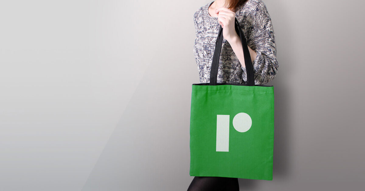 A woman holding a green colored handbag with custom business logo printed on it.