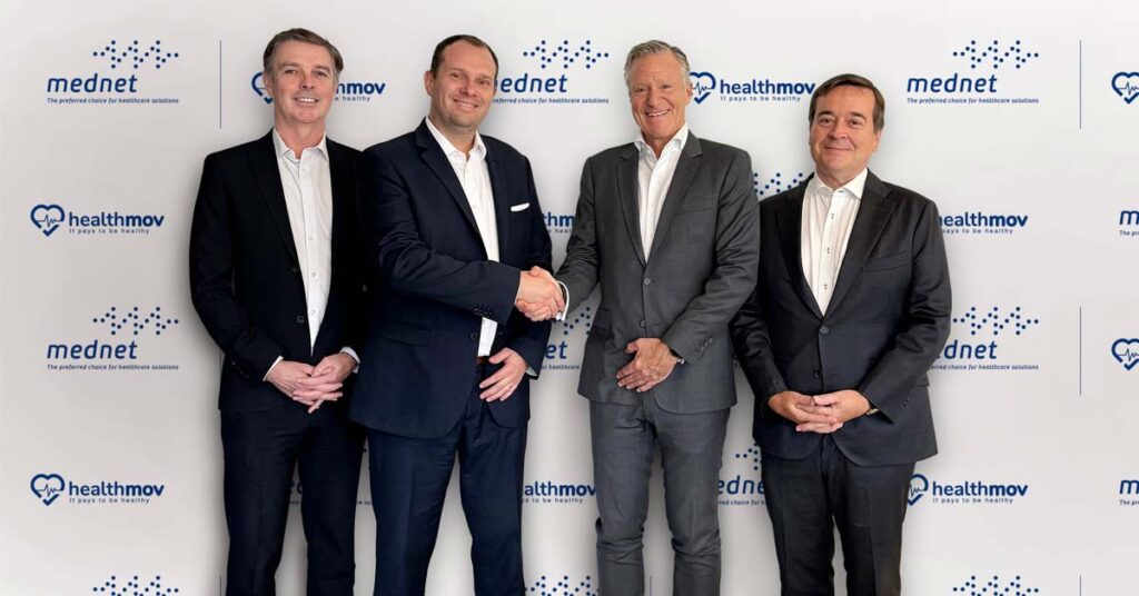 A group of 4 men in formal clothing standing in front of a background featuring the logos of UAE's MedNet and HealthMov on the occasion of their partnership