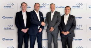 A group of 4 men in formal clothing standing in front of a background featuring the logos of UAE's MedNet and HealthMov on the occasion of their partnership