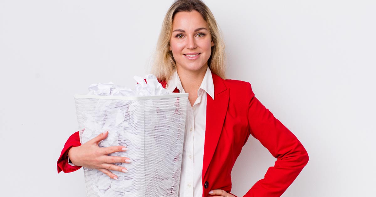 A white woman in red blazer holding a trash can full of waste paper