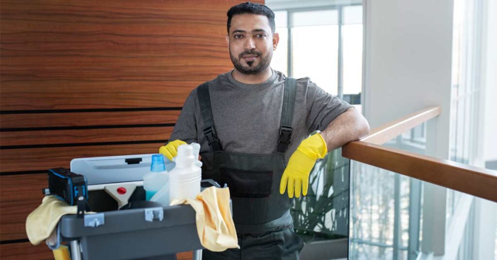 A smiling male janitor standing in an office environment