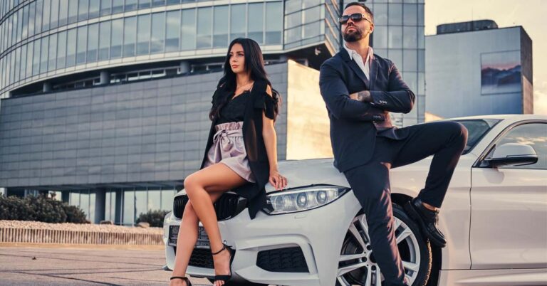 A man and woman sitting at the bonnet of their rented luxury white car.