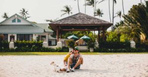 A happy smiling young father and little daughter sitting in front of a beachfront property with their dog pet.