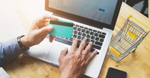 A picture depicting online payment concept, with a male person holding a credit card and operating on a laptop device.
