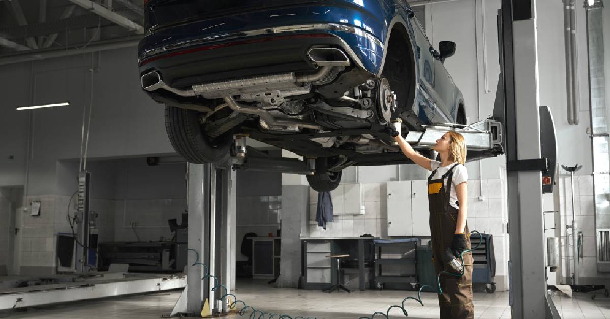 A woman worker operating a 2 post car lift, in a garage setting