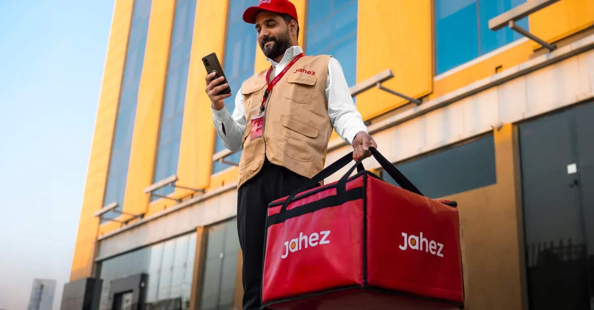 Jahez delivery executive holding smartphone and insulated delivery bag in front of company building