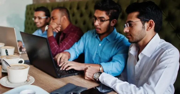 A group of young Indian men working on laptops in a cafe setting - depicting government startup loan application process