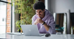 Young man smiling while working on a Dell laptop on a desk