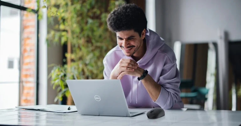 Young man smiling while working on a Dell laptop on a desk