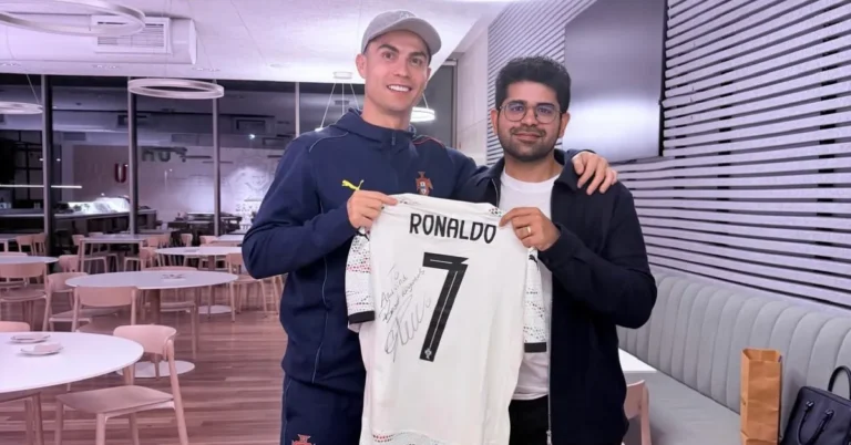 Cristiano Ronaldo, left, and Perplexity CEO Aravind Srinivas, right, hold a signed CR7 football jersey reading "To Arvind, Best Regards" during their AI investment partnership announcement.