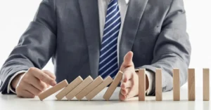 Businessman in a suit stopping wooden blocks from toppling in a domino effect, symbolizing risk prevention before fundraising
