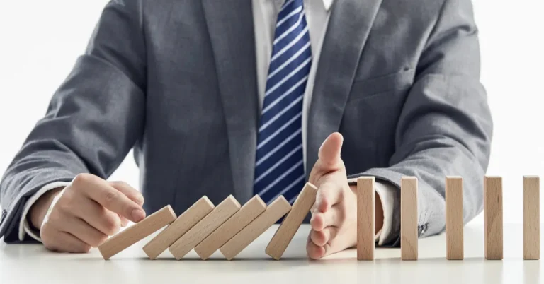 Businessman in a suit stopping wooden blocks from toppling in a domino effect, symbolizing risk prevention before fundraising