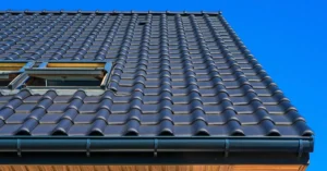 Open roof access hatch on a dark tiled pitched roof against a clear blue sky
