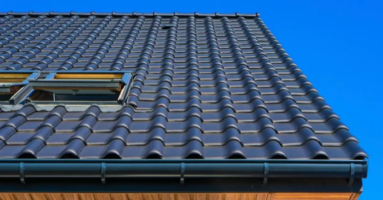 Open roof access hatch on a dark tiled pitched roof against a clear blue sky