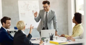 Business leader presenting to his team during a leadership meeting at a whiteboard in a modern office