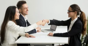 Two professionals shaking hands across a table while a third looks on, representing a startup finalising a new hire