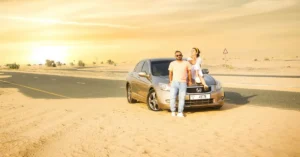 Couple leaning on a sedan on a desert road in Dubai at sunset