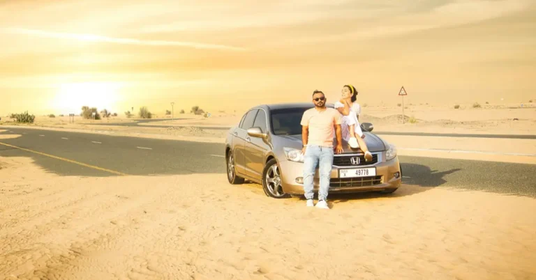 Couple leaning on a sedan on a desert road in Dubai at sunset