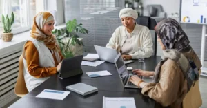 Three female colleagues working at a meeting table with laptops, a tablet and documents in a modern office