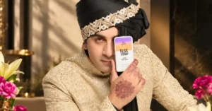 Ranbir Kapoor in a black turban and gold embroidered sherwani holds Flux Theory The Lover Glow Body Wash beside his face