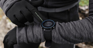 Hiker in gloves tapping a black digital sports watch with a blue bezel on a rocky trail